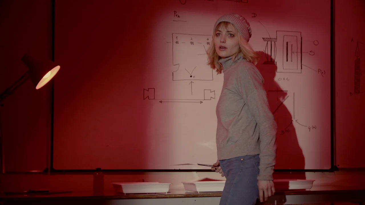 Live-action woman in a knitted hat standing in a red-lit room